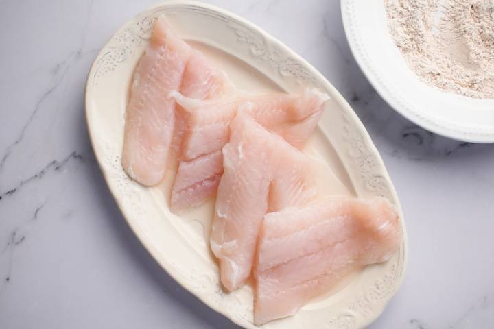 Cod fish filets on a plate with flour on the side.