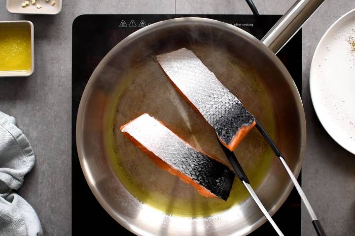 Salmon cooking with the flesh side down in a pan.