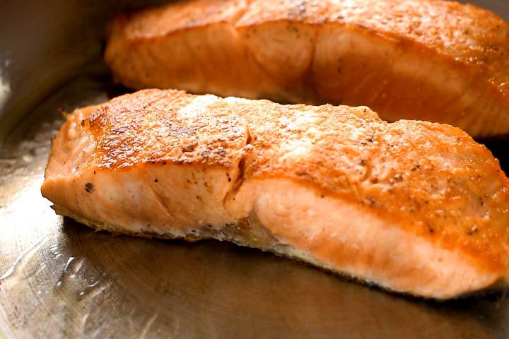 Salmon being seared in a pan with the skin side down.
