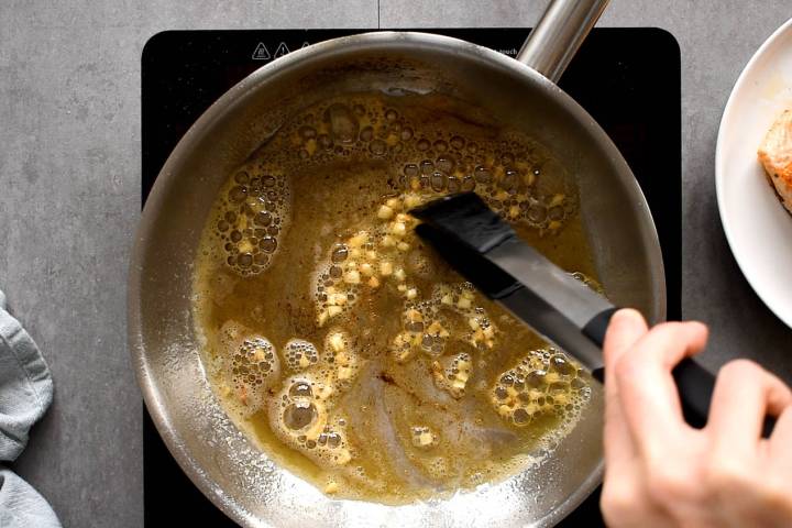 Butter and garlic cooking in a pan with tongs.