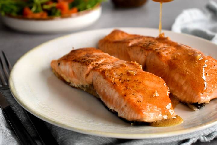 Garlic lemon butter sauce being poured over salmon on a plate.