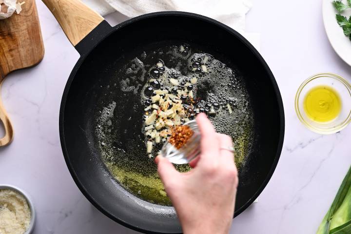 Garlic and red pepper flakes being added to butter and olive oil in a pan.