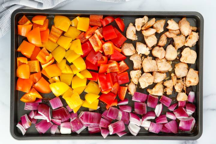 Yellow, red, and orange bell peppers with red onions and chicken breast on a baking sheet.