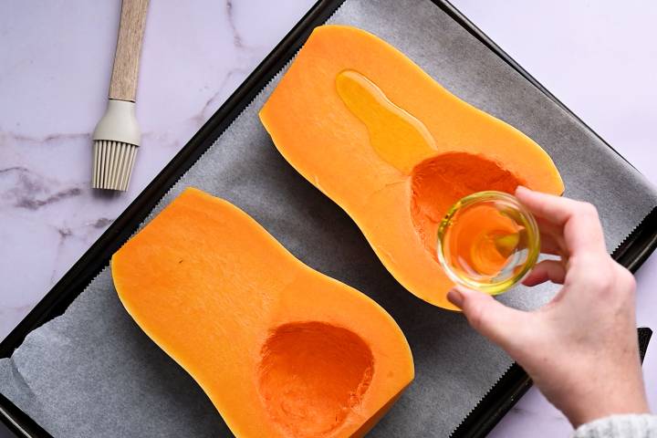 Olive oil being drizzled over butternut squash halves.