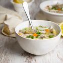 Slow cooker lemon artichoke chicken soup with rice in a bowl with carrots and lemon.