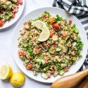 Quinoa tabbouleh with lentils, cucumbers, tomatoes, and parsley served on two plates with lemon.