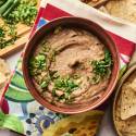 A bowl of creamy refried beans is garnished with chopped green onions and cilantro, served alongside tortilla chips on a colorful napkin.