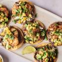 A plate of six shrimp tostadas with black beans, shredded cabbage, corn, avocado, and cilantro.