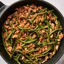 Ground turkey and green bean stir fry in a skillet with spicy sauce and chopsticks.