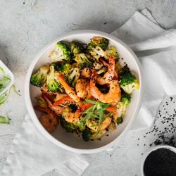 A top-down shot of a bowl of firecracker shrimp and broccoli, garnished with scallions and sesame seeds.