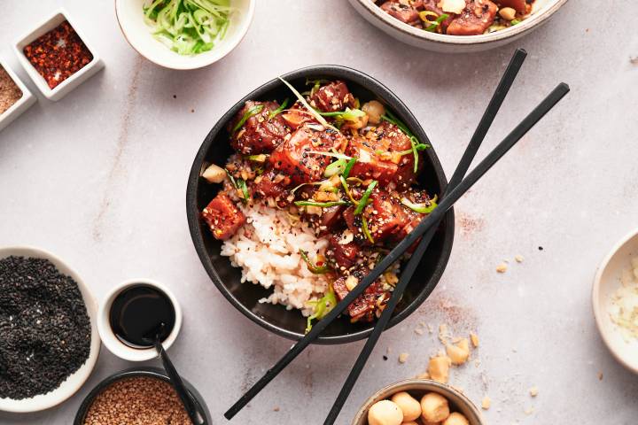 Ahi tuna poke with raw tuna, onion, soy sauce, sesame seeds, green onions, and seaweed in a bowl.