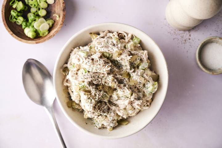 A bowl of dill pickle chicken salad on a wooden board.