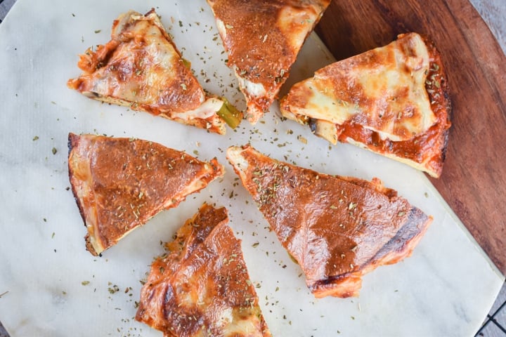 Pizza frittata with tomato sauce and melted cheese cut into slices on a cutting board.