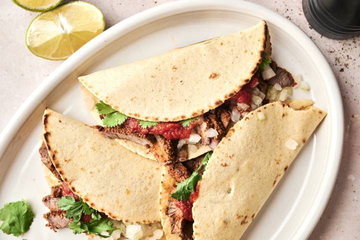 Overhead view of assembled steak tacos filled with grilled beef, onions, salsa, and fresh cilantro on a white oval platter.
