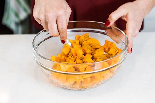 Adding spices to a glass bowl with sweet potato and butternut squash.