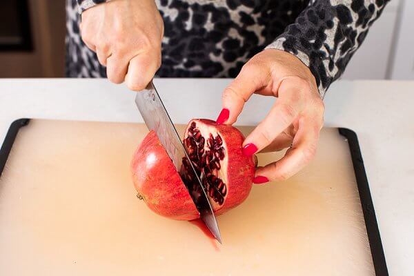 Liz cutting a pomegranate in half with a large, sharp knife on a cutting board.