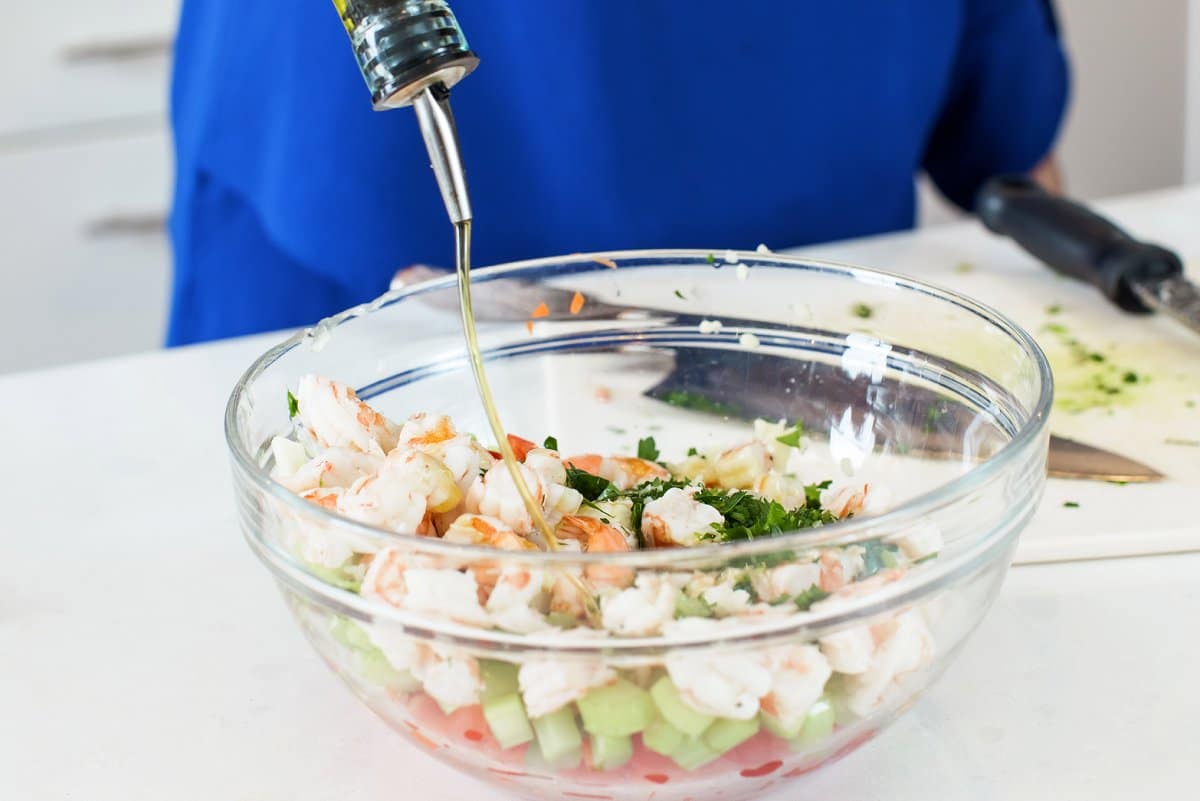 olive oil being poured on shrimp salad