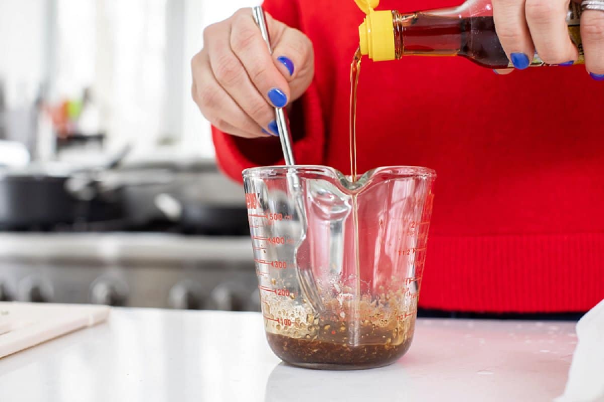Drizzling sesame oil into a liquid measuring cup and stirring with a fork.