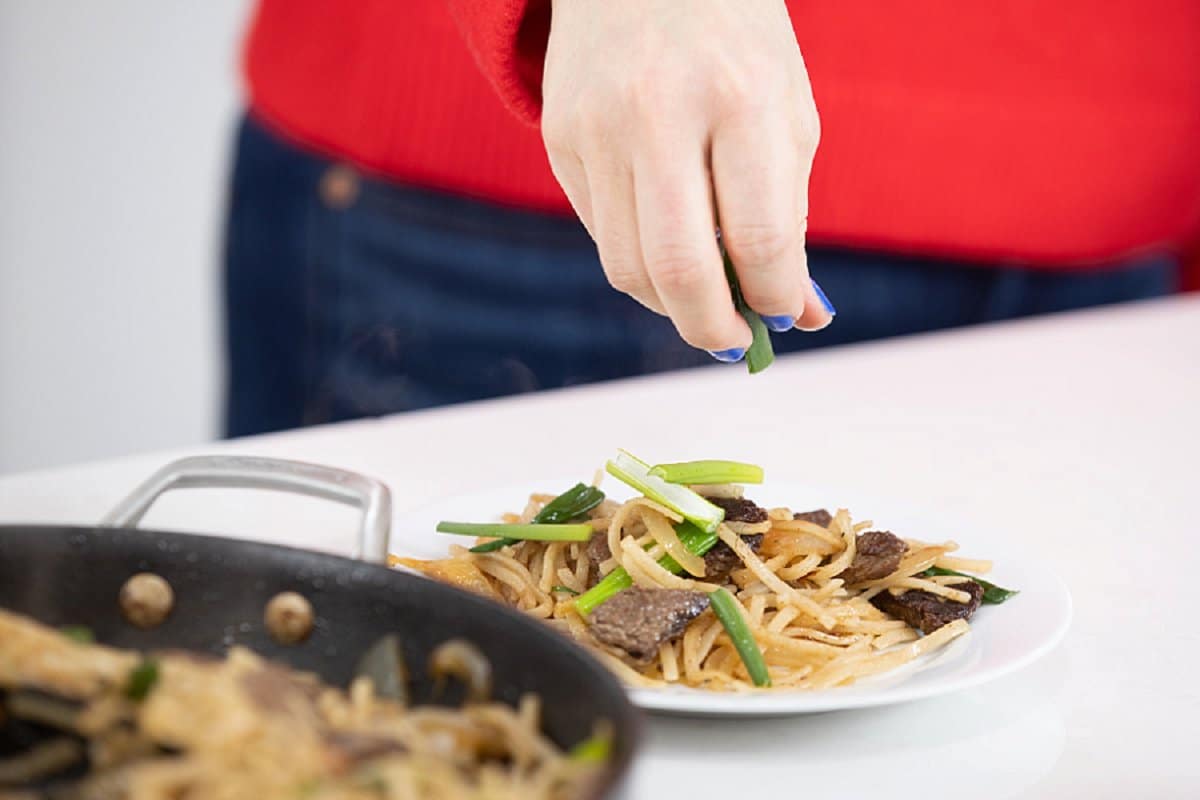 Garnishing a serving of beef stir-fry with rice noodles on a plate.