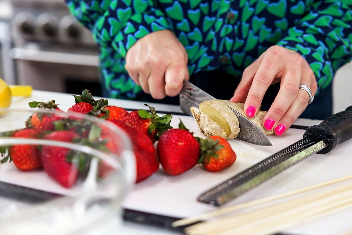 Liz cutting fresh ginger with berries on a cutting board.