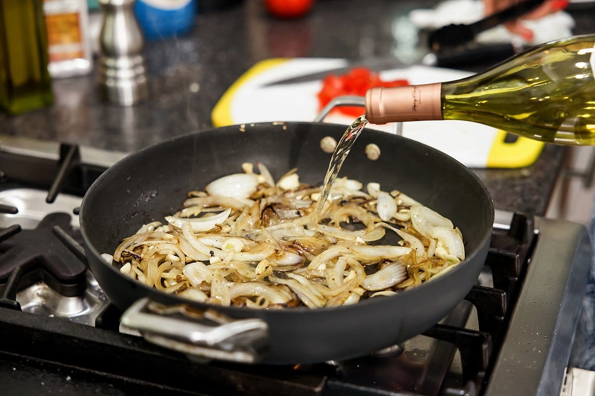 Onions being sautéed in a pan with white wine