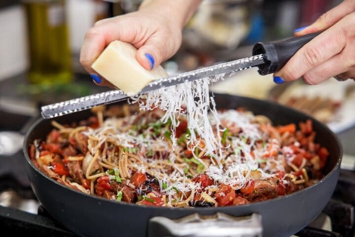 garnishing sausage and peppers pasta with cheese
