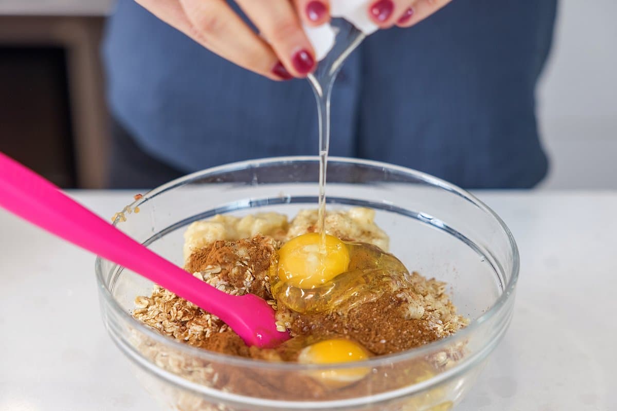 Adding eggs to pancake batter in glass bowl.