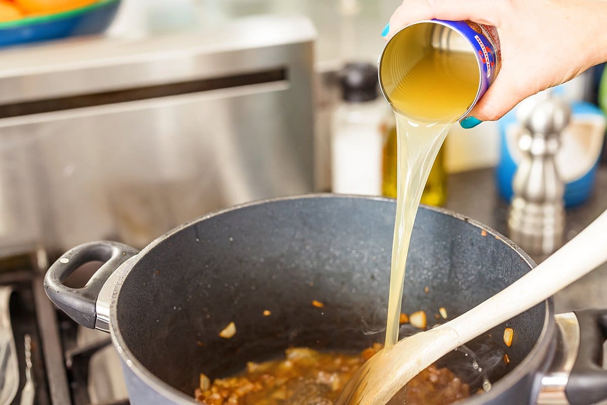 Pouring canned chicken broth into a pot.