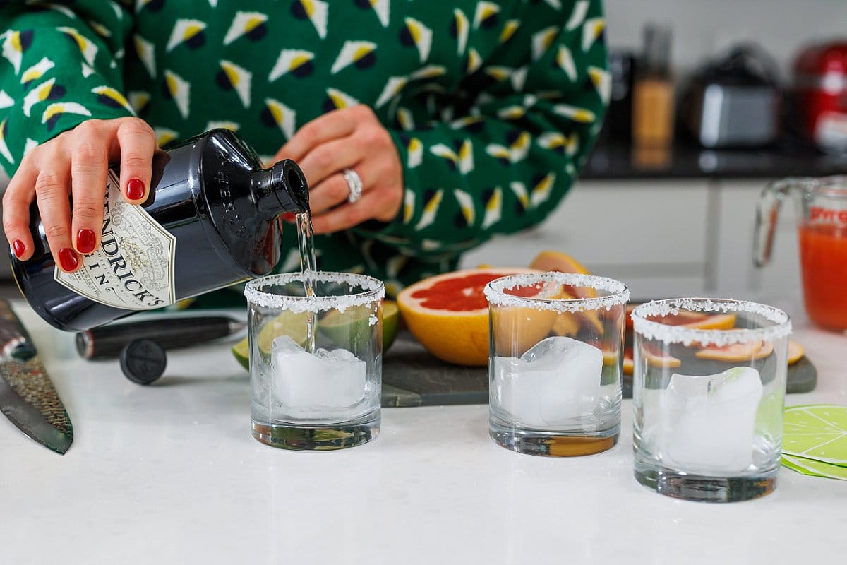 Pouring gin into glass tumblers over ice.