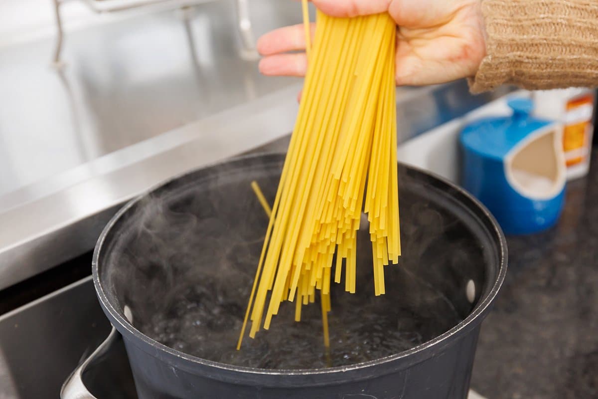 Adding linguine to pot of boiling water.