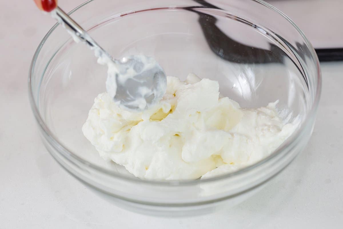 Dolloping Greek yogurt into a glass bowl.