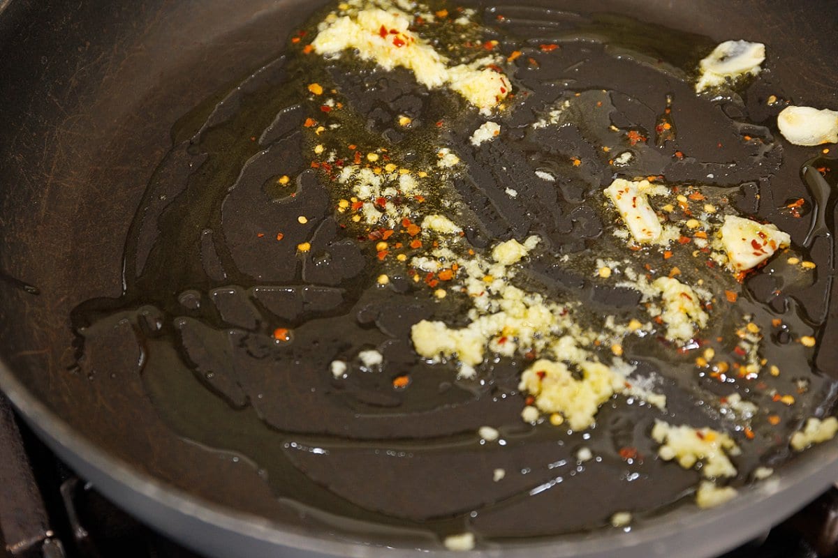 Garlic and chili flakes sautéing in a large pan in oil.