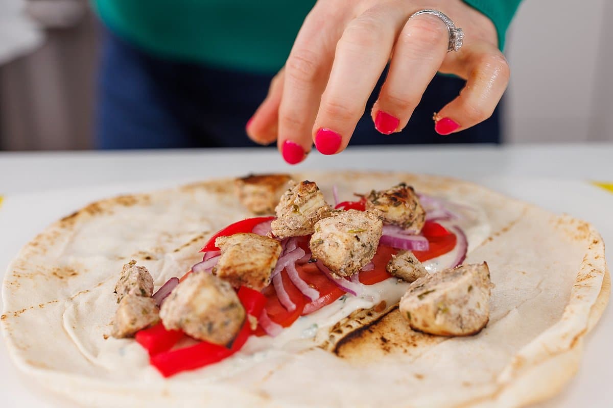 Adding chicken shawarma, red onion, and bell pepper to pita wrap.