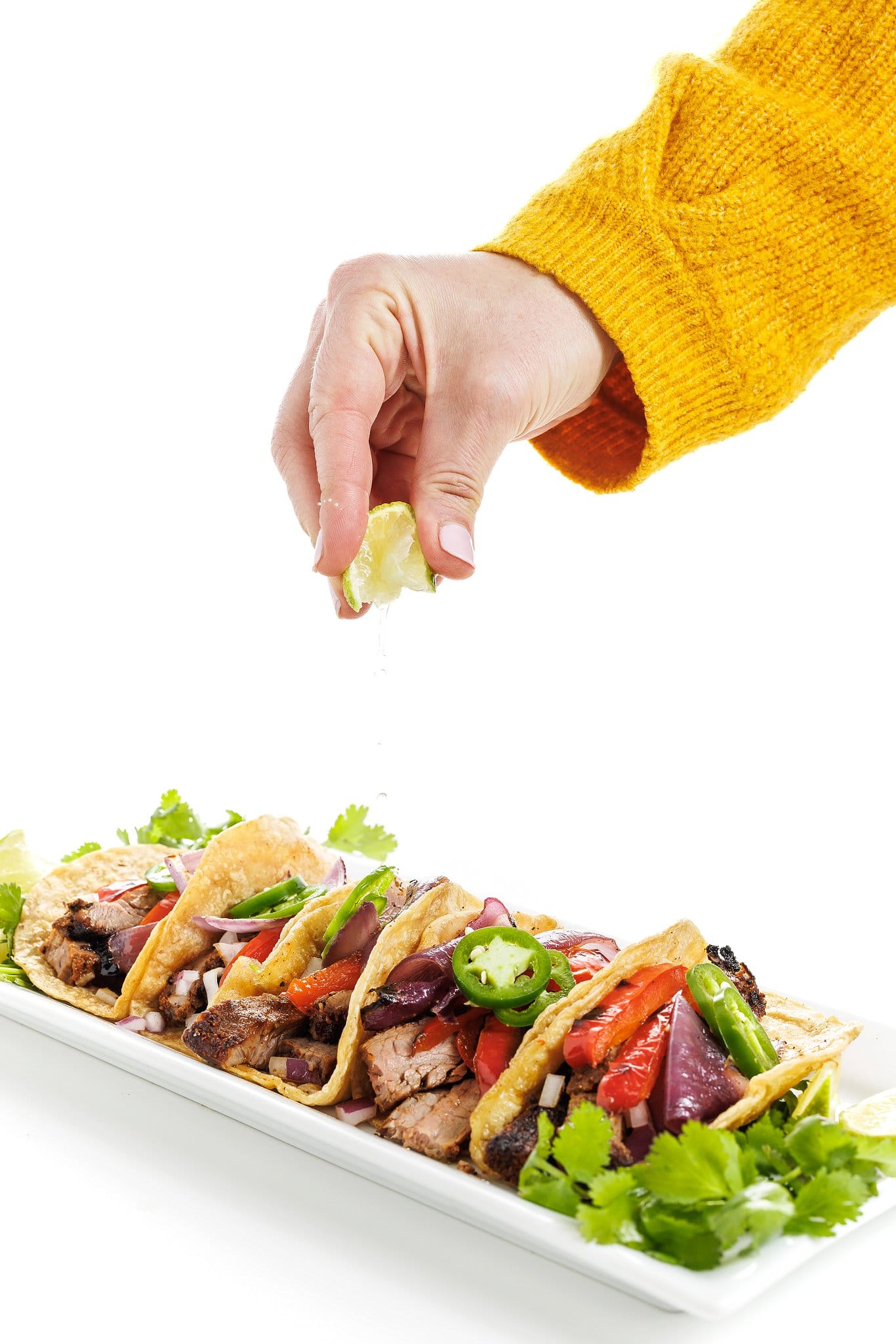 Garnishing flank steak tacos with fresh lime juice.