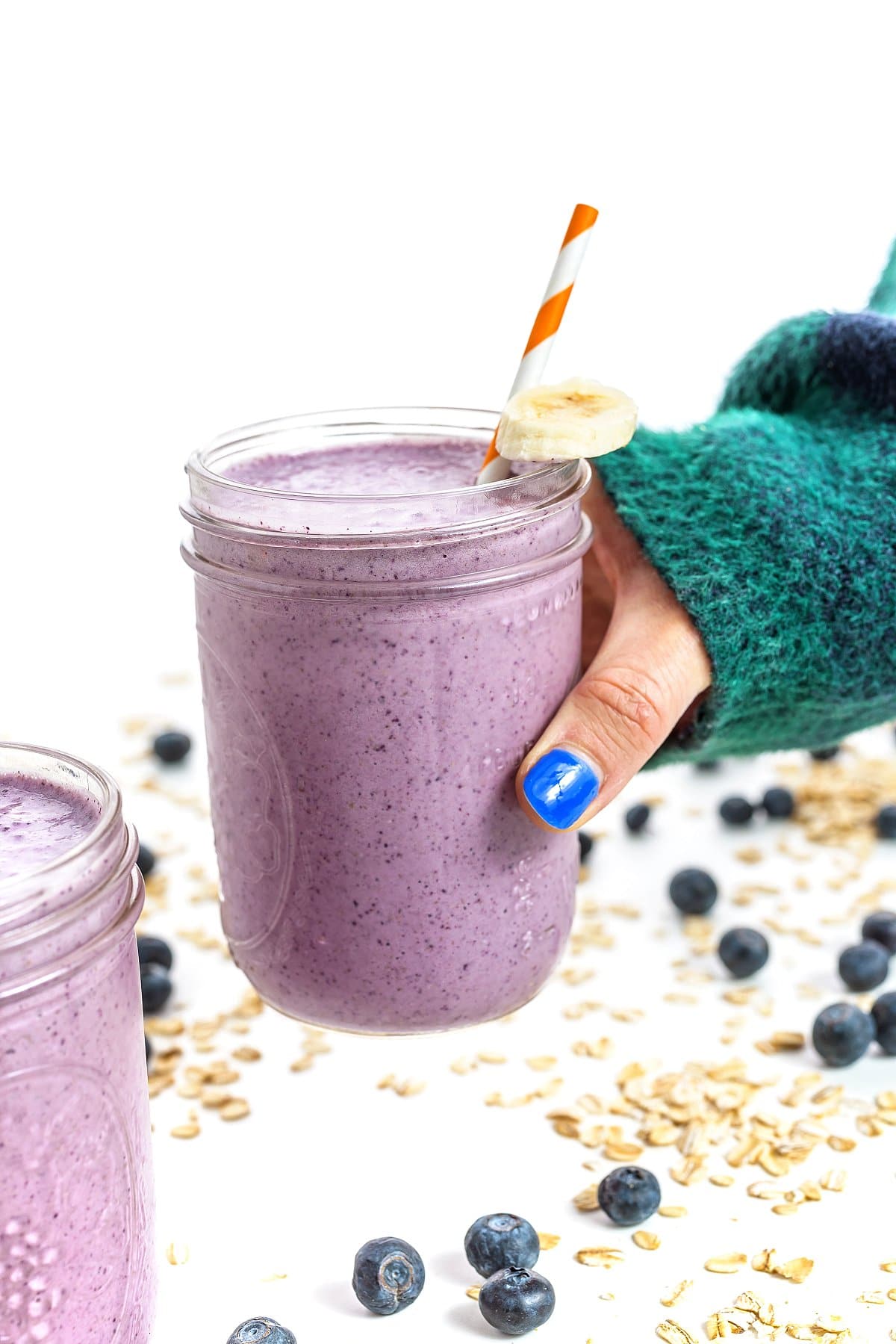 Holding a glass full of blueberry banana oatmeal smoothie.