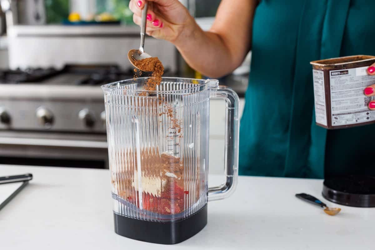 Liz sprinkling cocoa powder into blender.