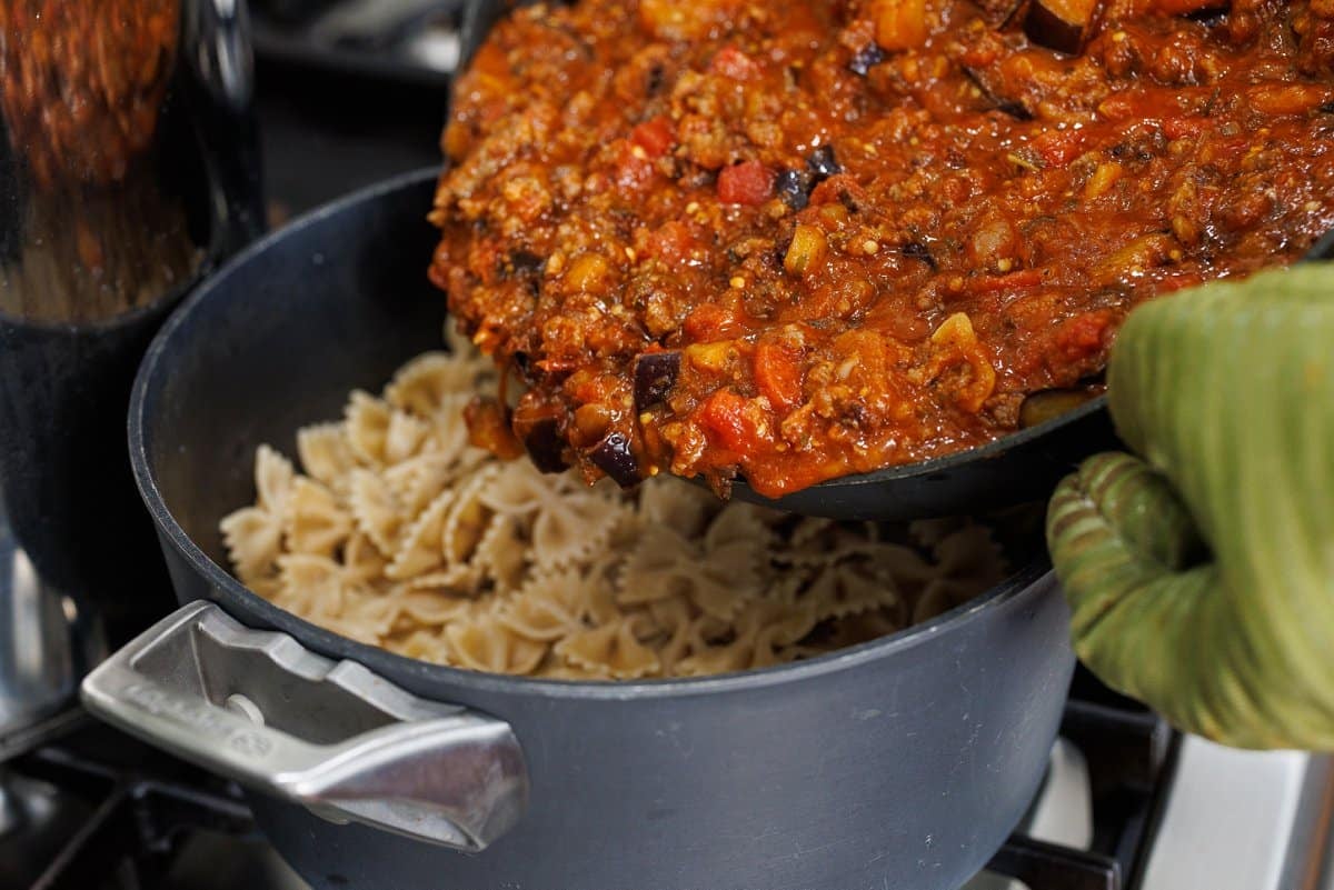 Pouring eggplant, sausage, tomato sauce over top cooked pasta.
