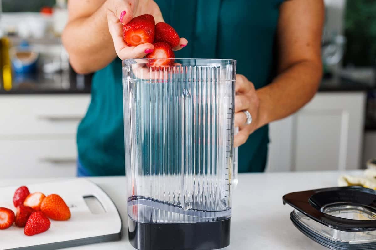 Liz adding halved strawberries to a blender.