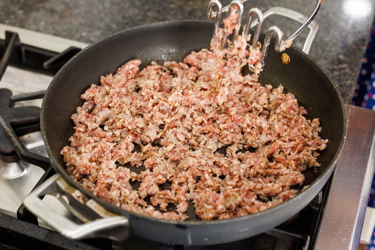 Browning ground sausage in a large skillet on the stove.
