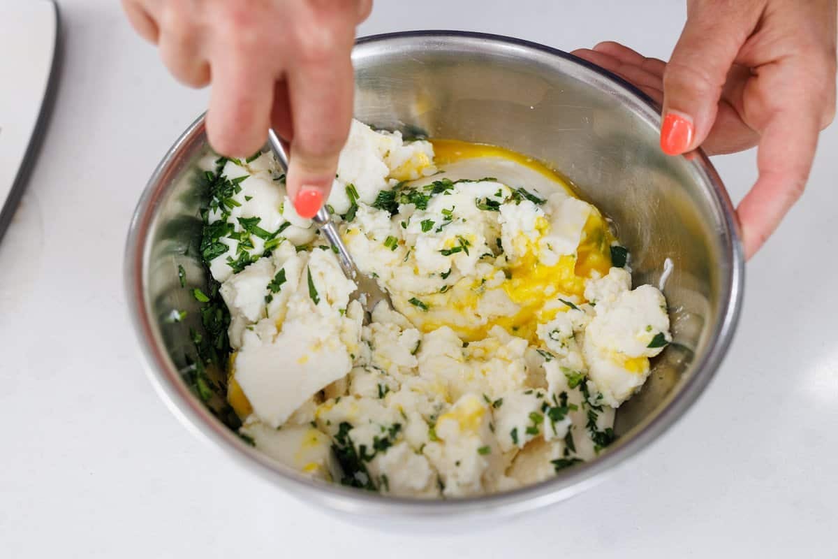 Using a fork to mix ricotta cheese, egg, and fresh herbs.