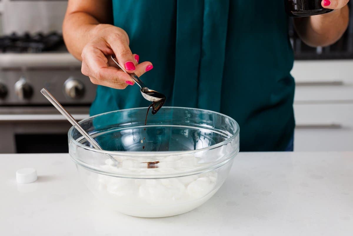 Adding vanilla to yogurt in glass bowl.