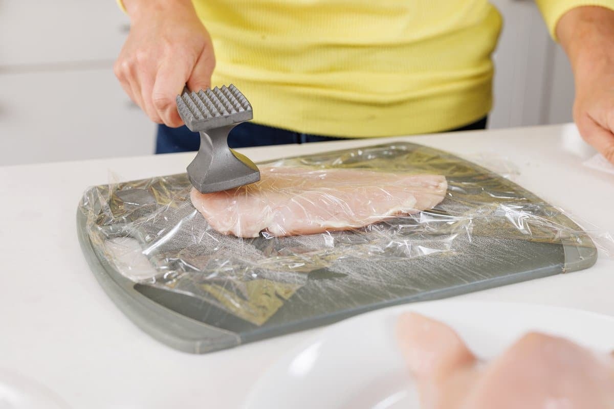 Pounding chicken thinner with a meat mallet.