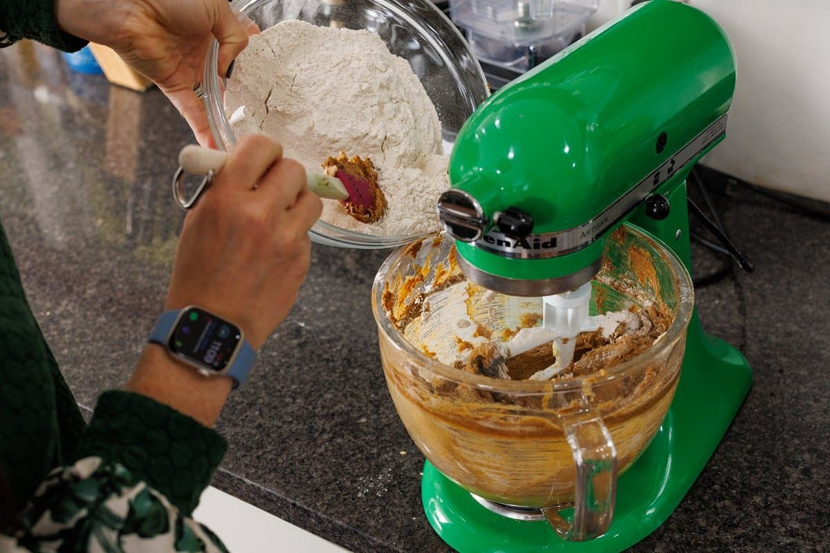 Pouring flour mixture into the bowl of a stand mixer with wet batter.