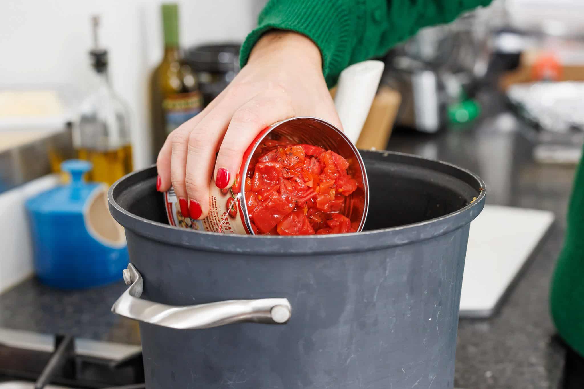Adding canned tomatoes to soup pot.