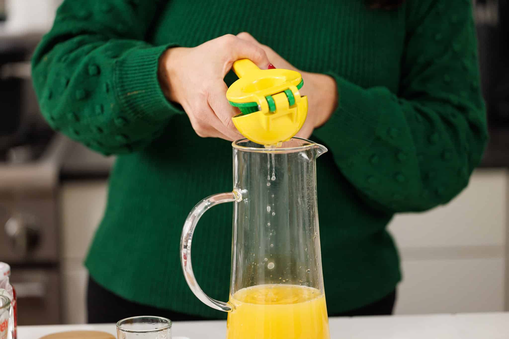 Using a citrus juicer to squeeze fresh lime juice into pitcher of hurricane cocktail.