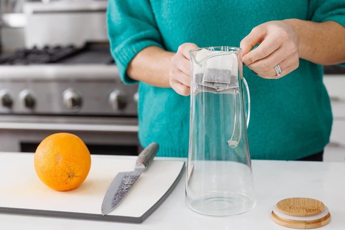 Adding tea bags to a large glass pitcher.