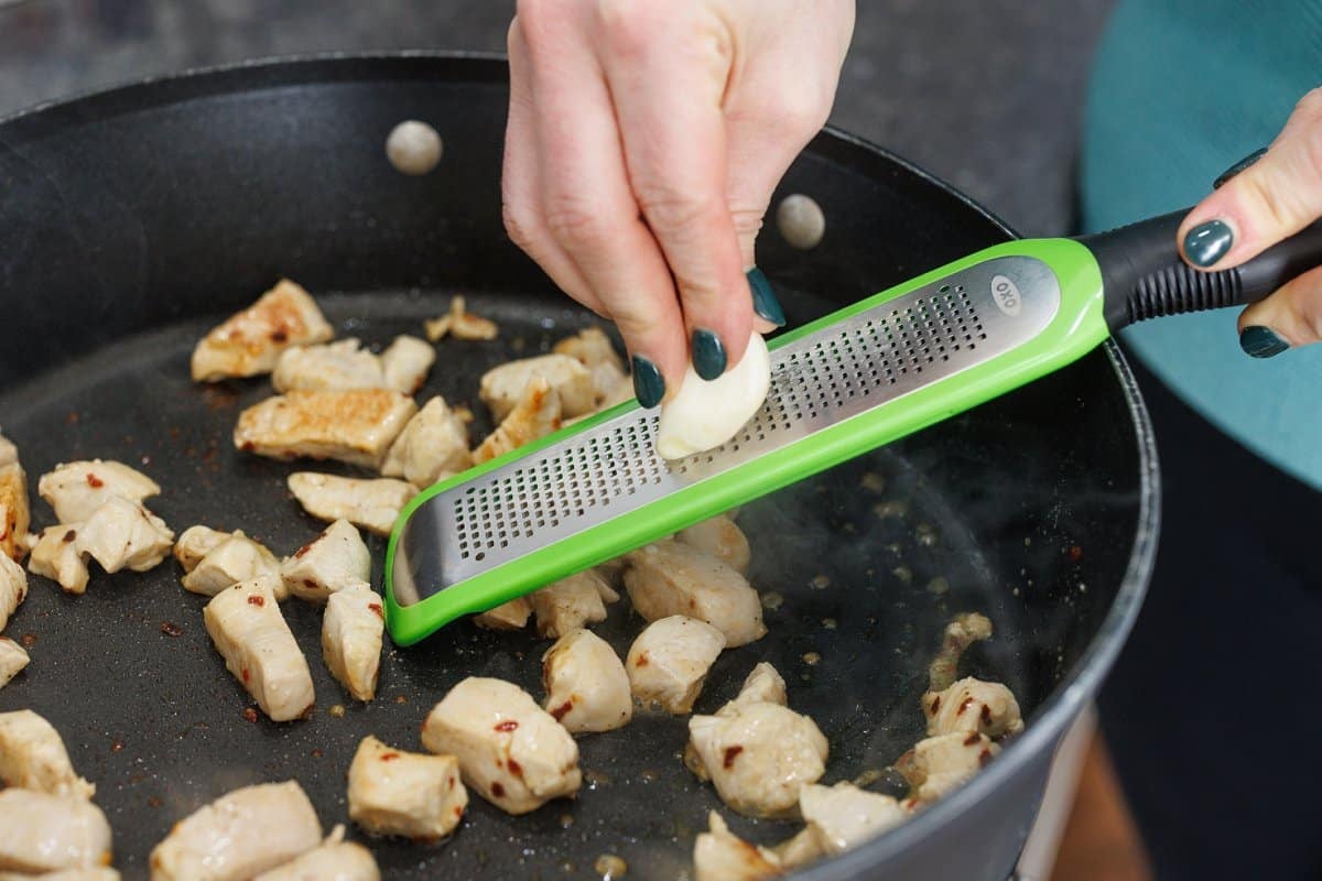Grating a garlic clove with a microplane into skillet.