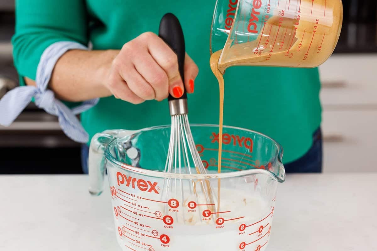 Pouring melted peanut butter into milk mixture in measuring bowl.