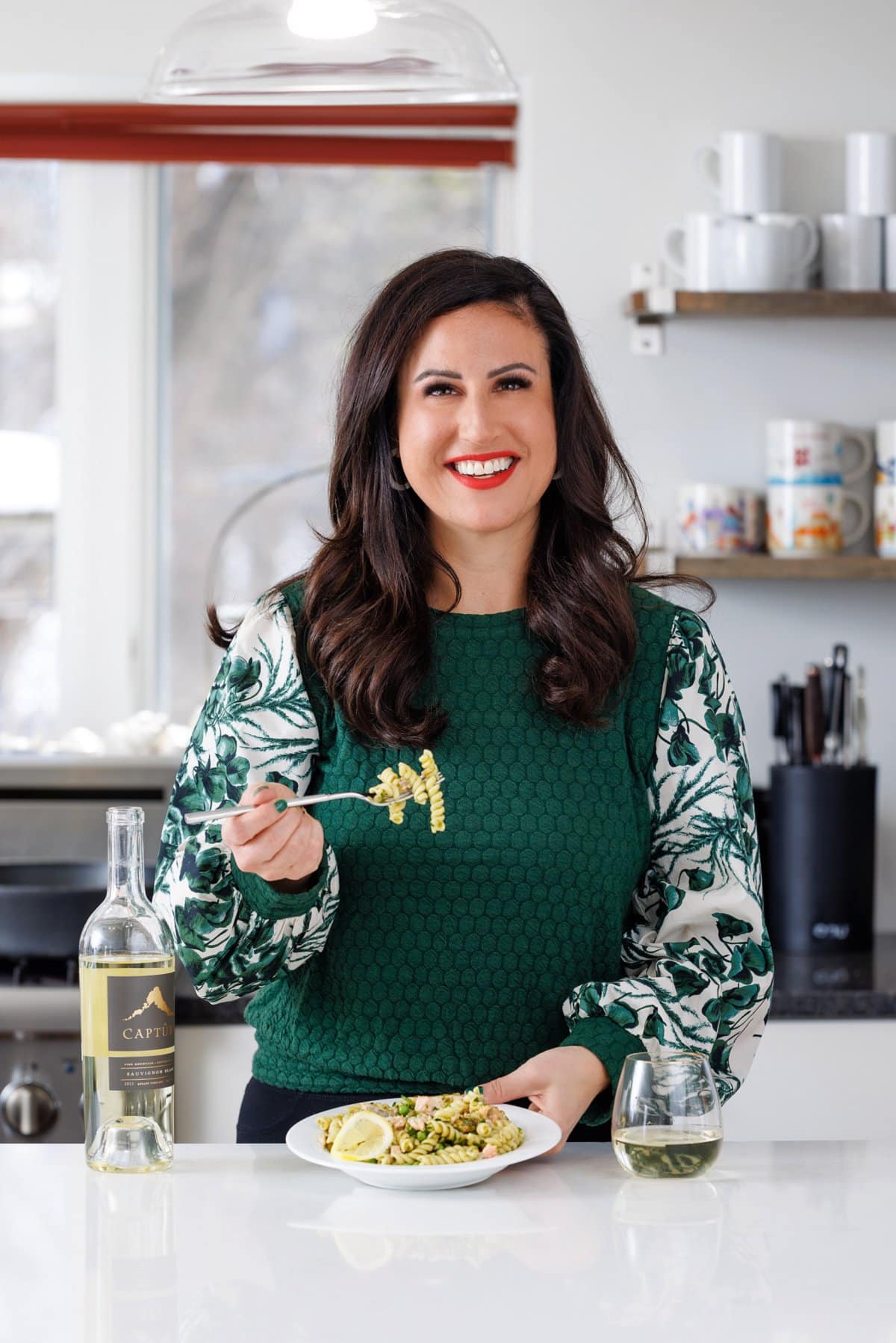 Liz eating pesto pasta with salmon and peas with a glass of Capture Wine.