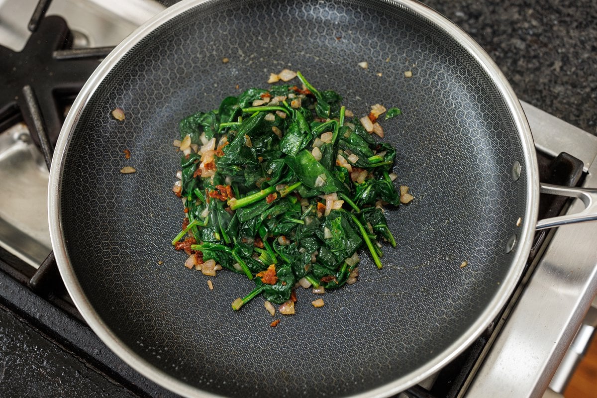 Wilted spinach, onion, and sun-dried tomato in a pan.
